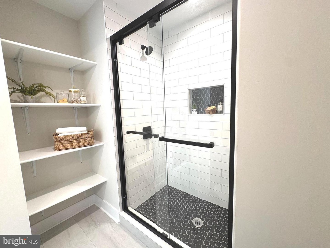 Glass shower with black tile floor and open shelving